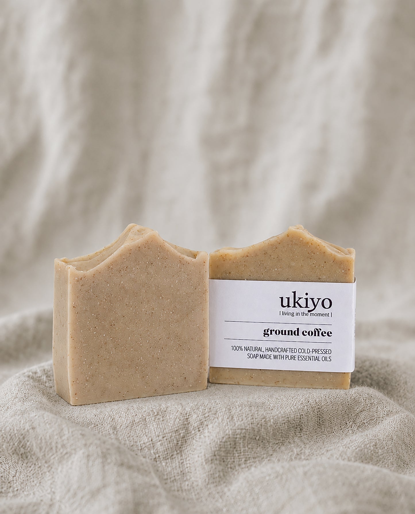 Two bars of ground coffee soap with a label on a textured beige background