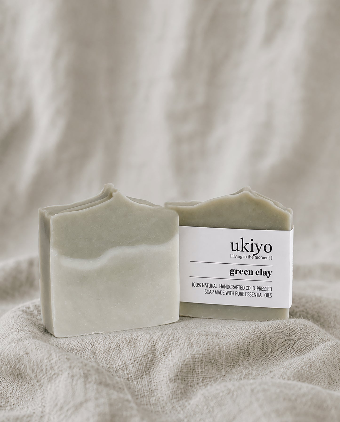 Bar of green clay soap with a 'ukiyo' label on a beige fabric background