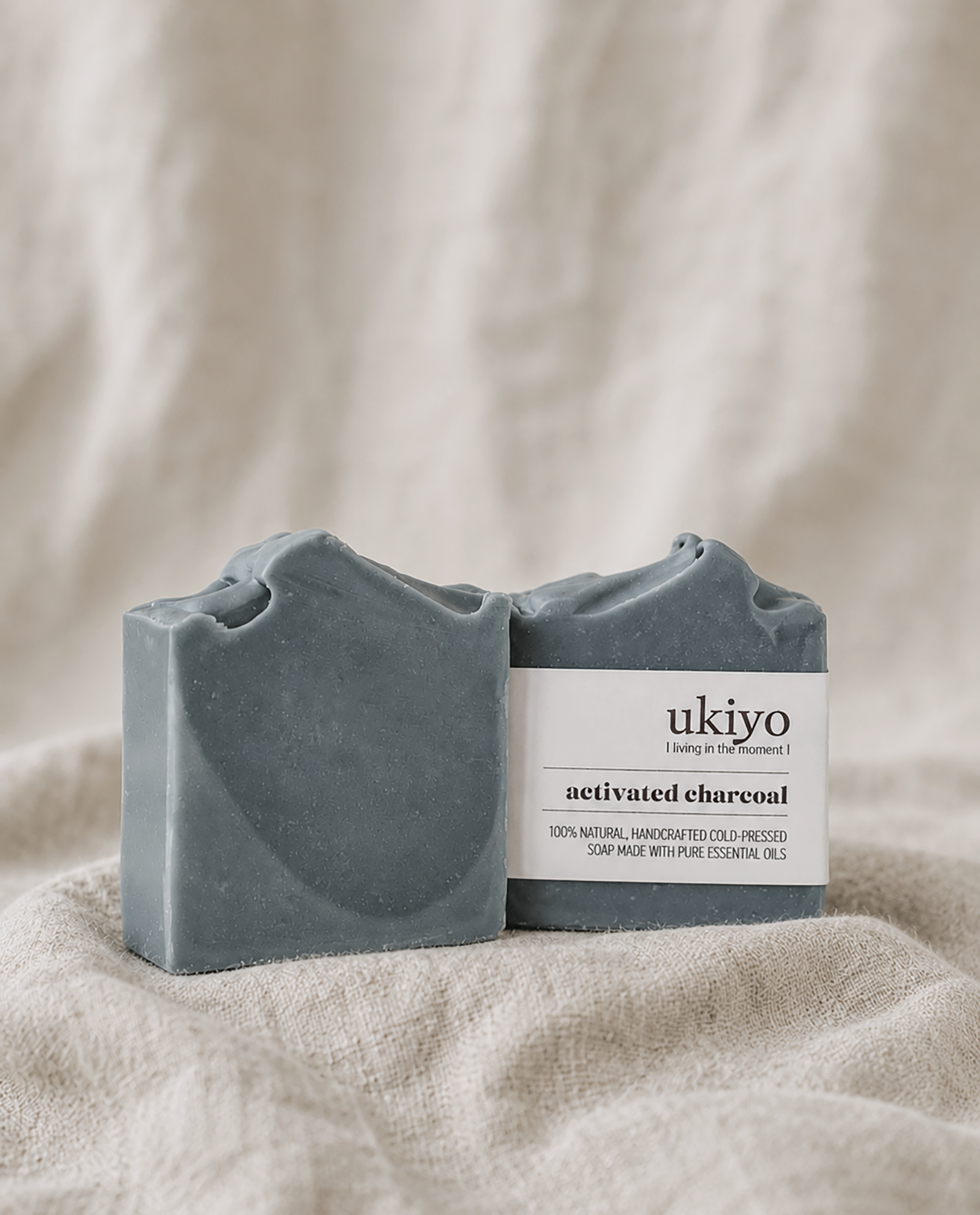 Two bars of activated charcoal soap with a 'ukiyo' label on a beige fabric background