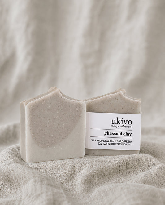 Bar of red clay soap and its packaging labeled 'ukiyo' on a textured beige background