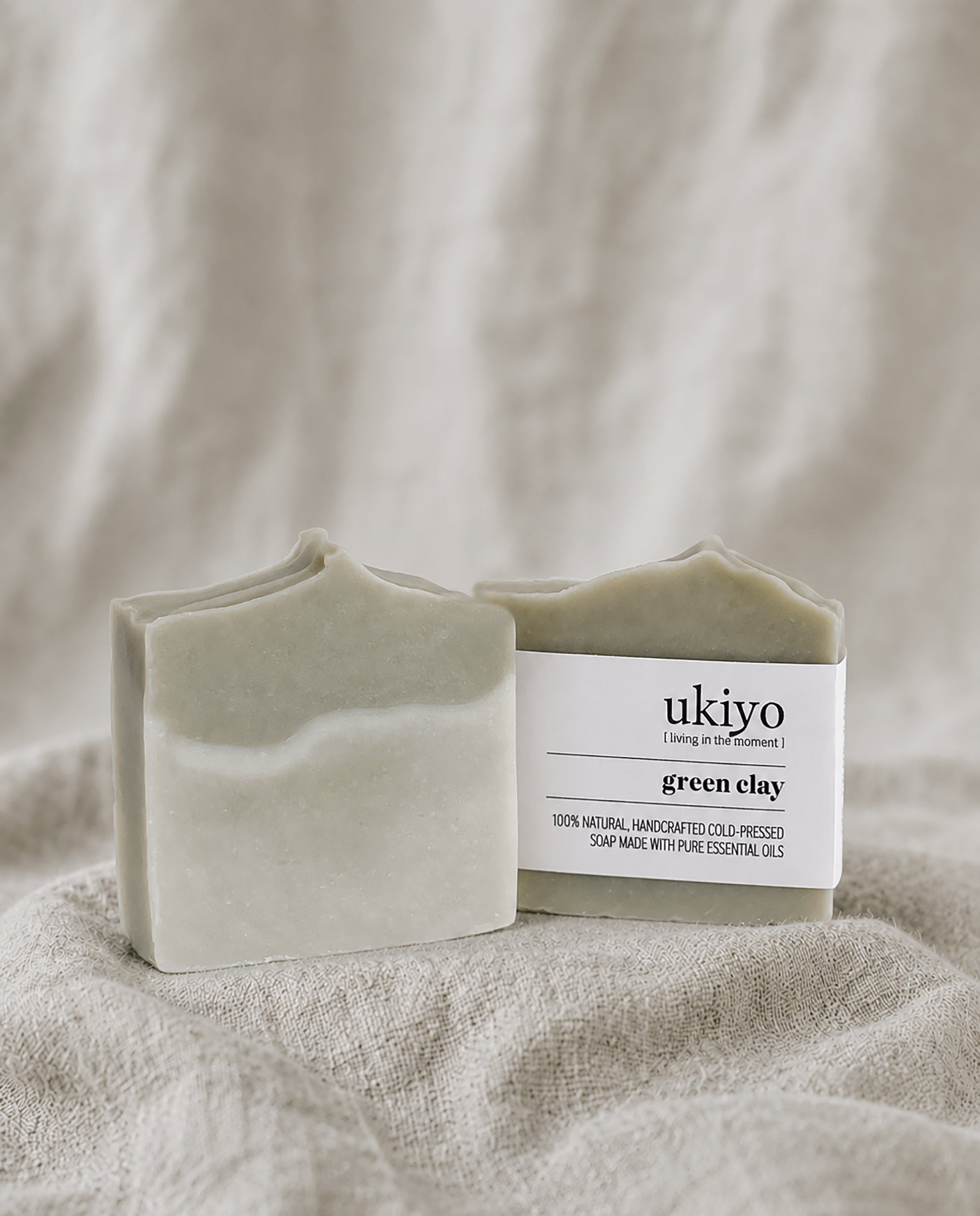 Bar of green clay soap with a 'ukiyo' label on a beige fabric background