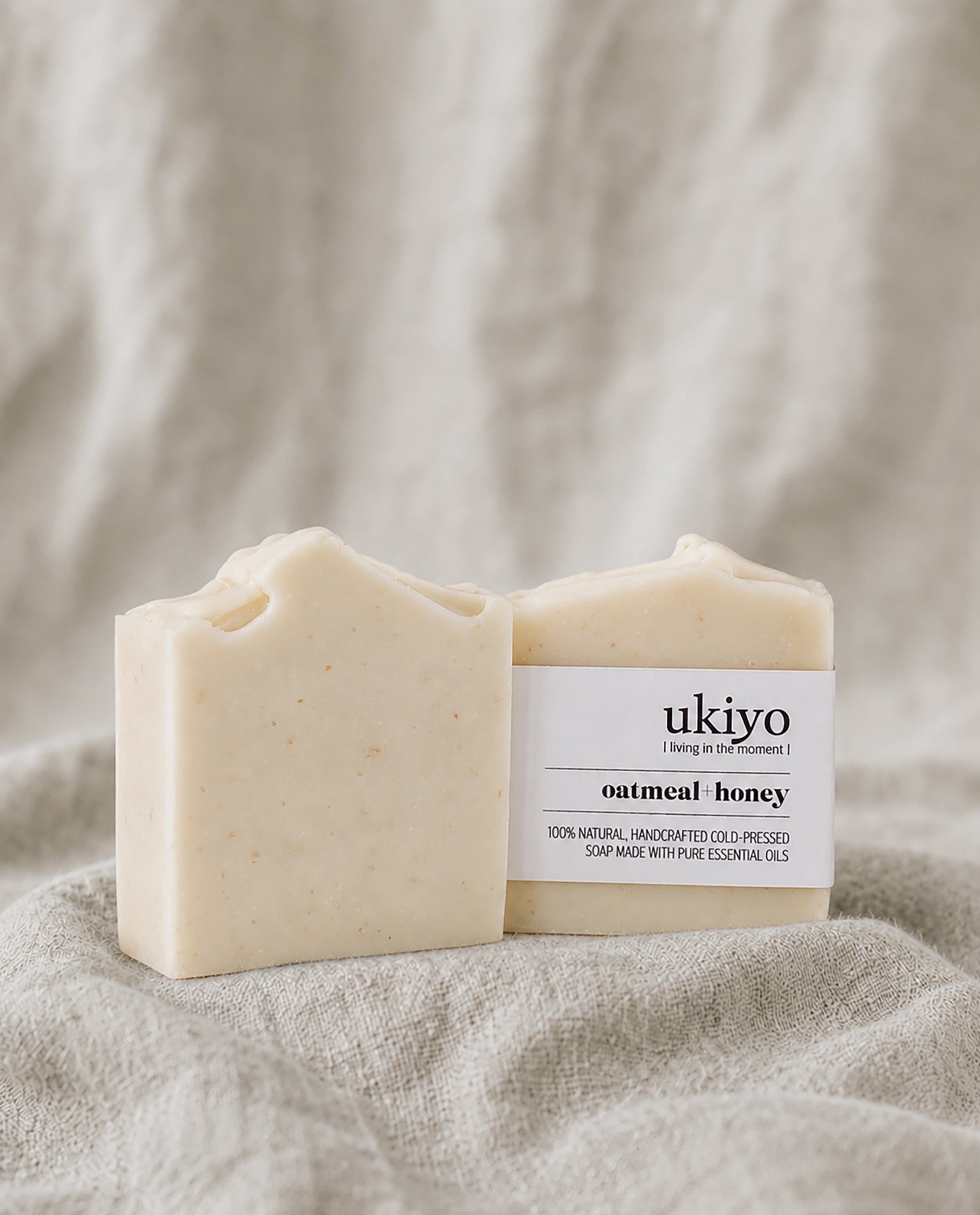 Two bars of oatmeal and honey soap with a 'ukiyo' label on a textured beige background