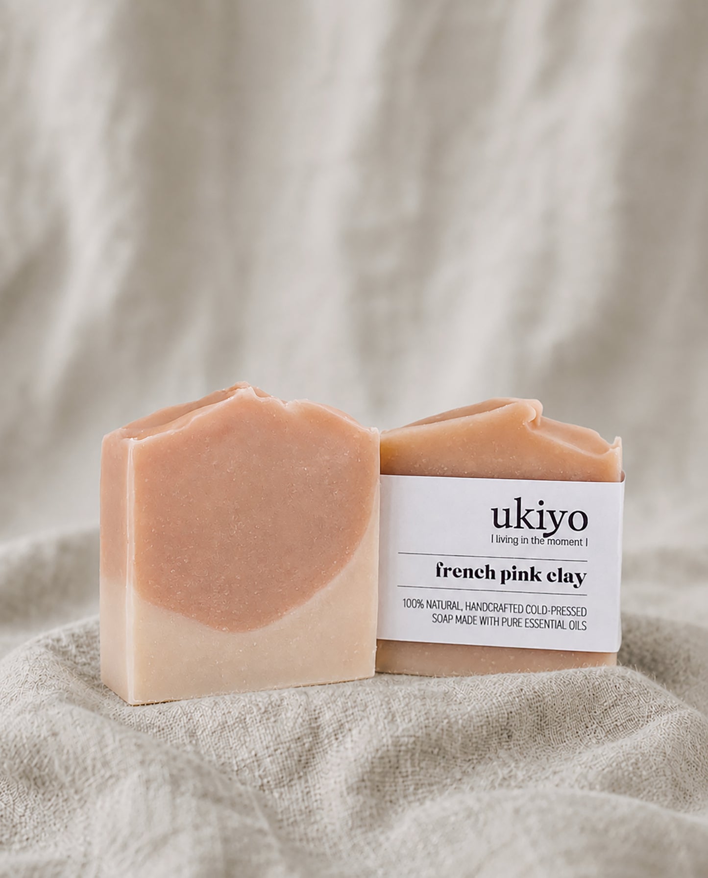 Bar of pink clay soap and its packaging labeled 'ukiyo' on a beige fabric background