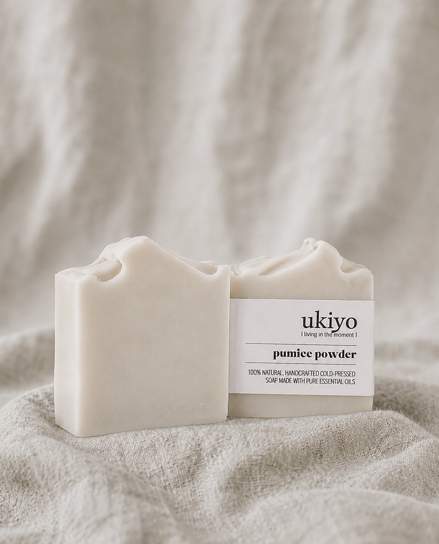 Two bars of pumice powder soap with 'ukiyo' branding on a textured beige fabric background