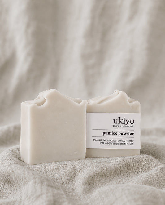 Two bars of pumice powder soap with 'ukiyo' branding on a textured beige fabric background