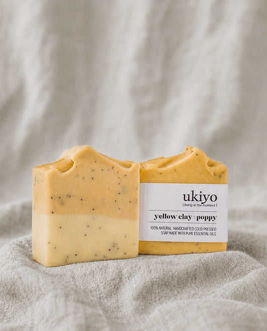 Yellow clay and poppy seed soap bar with a white label on a textured beige background